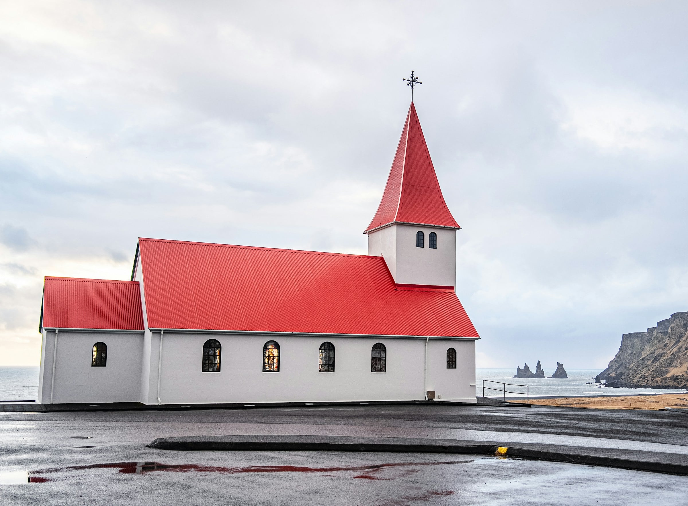 Vík í Mýrdal church with its red roof, Reynisdrangar sea stacks in the distance